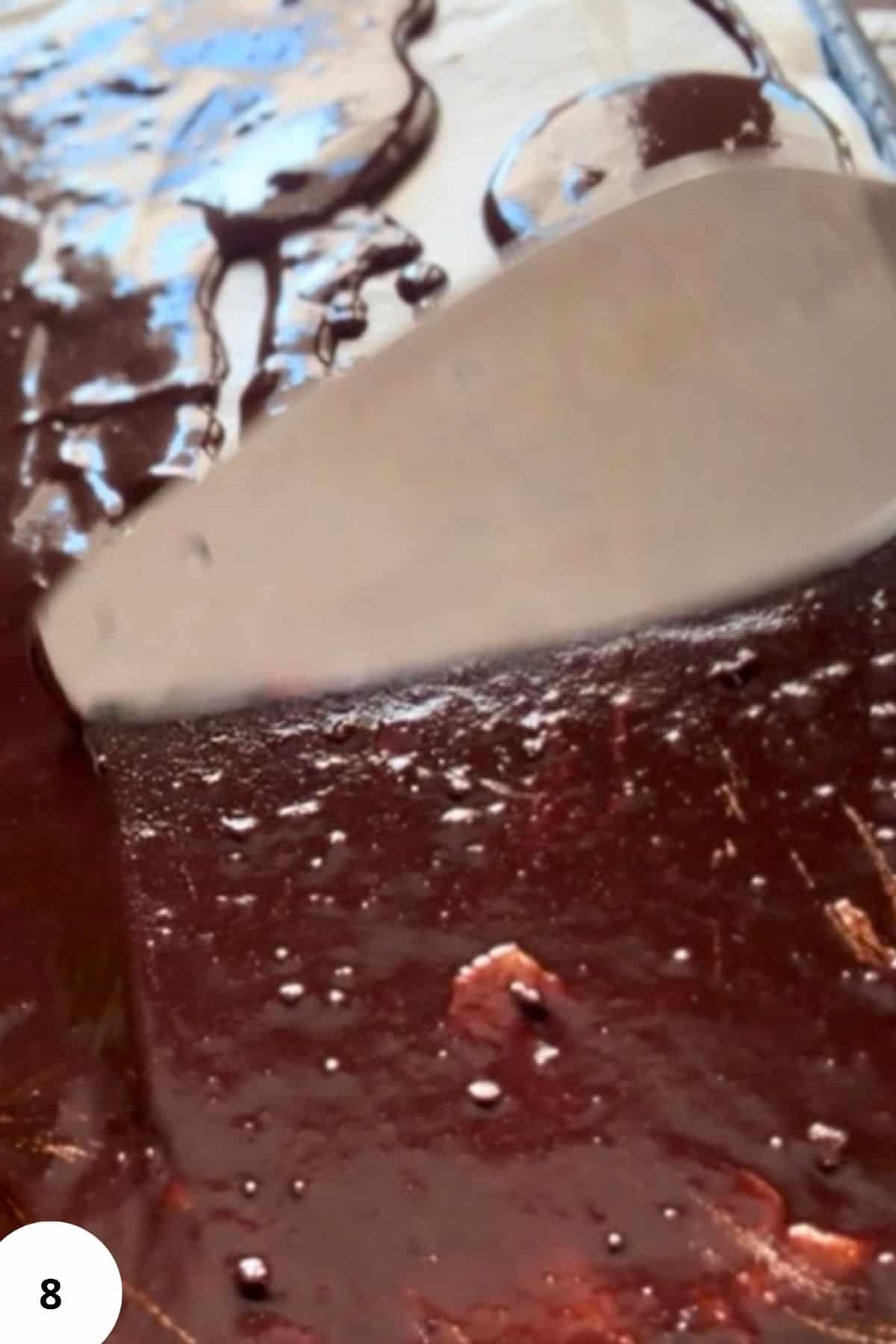 A cake server spreading glossy melted chocolate over the top of the cake in smooth.