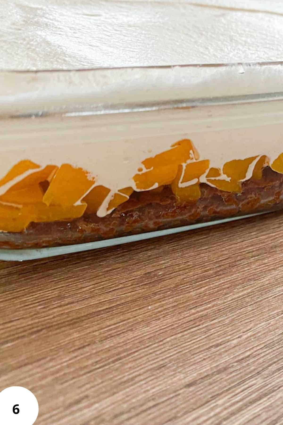 Finished Špikov Vrh cake served in a baking dish, with visible layers of soaked chocolate sponge, peaches, cream, and glossy chocolate glaze.