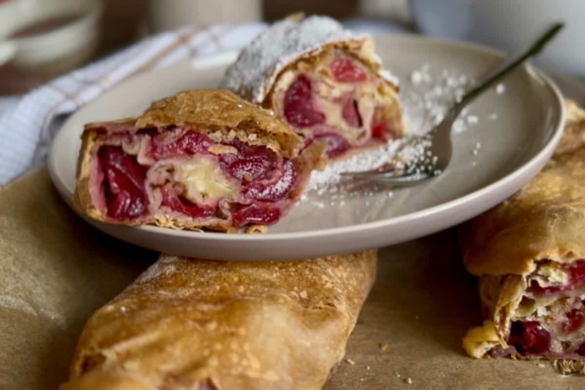A slice of cherry strudel served on a plate, showing the interior layers of cherries, breadcrumbs, and flaky pastry.