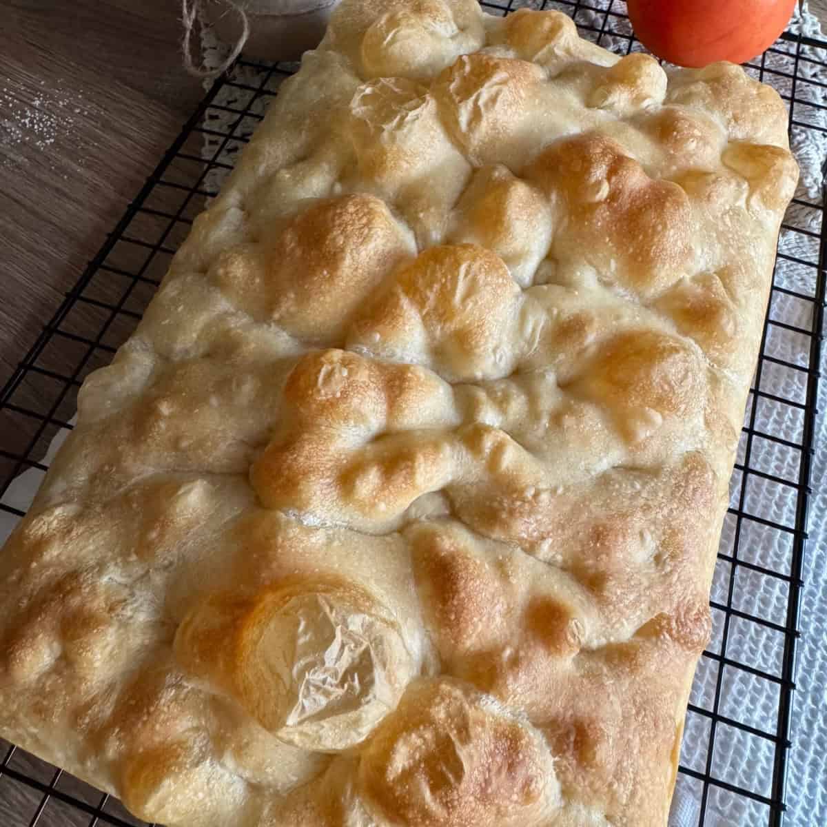 Freshly baked sourdough focaccia resting on a wire cooling rack.