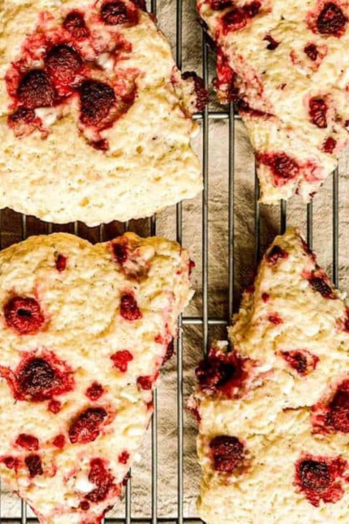 Raspberry sourdough scones resting on a cooling rack, showing their golden edges and scattered raspberry pieces.
