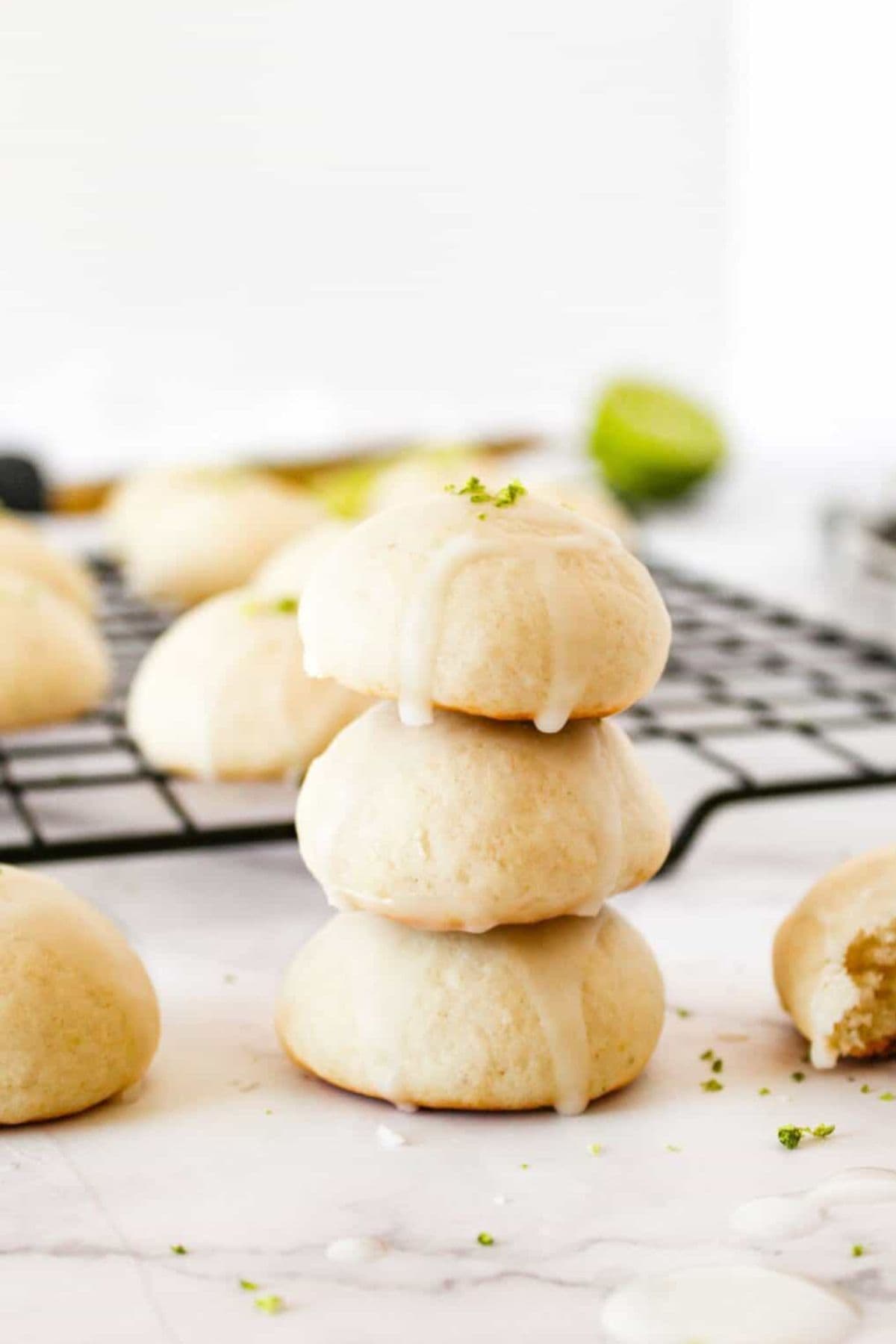 Three layers of ricotta cookies stacked in the foreground, with more cookies cooling on a wire rack in the background.
