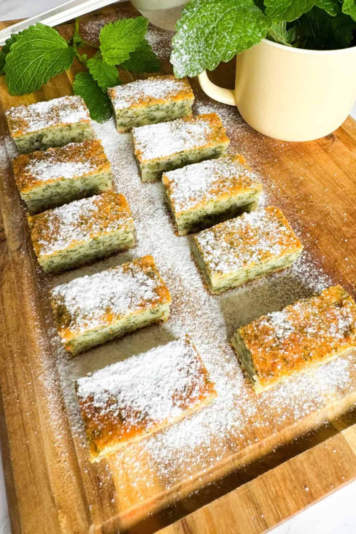 Lemon balm sheet cake made with sourdough discard, sliced and sprinkled with powdered sugar, served on a wooden board.