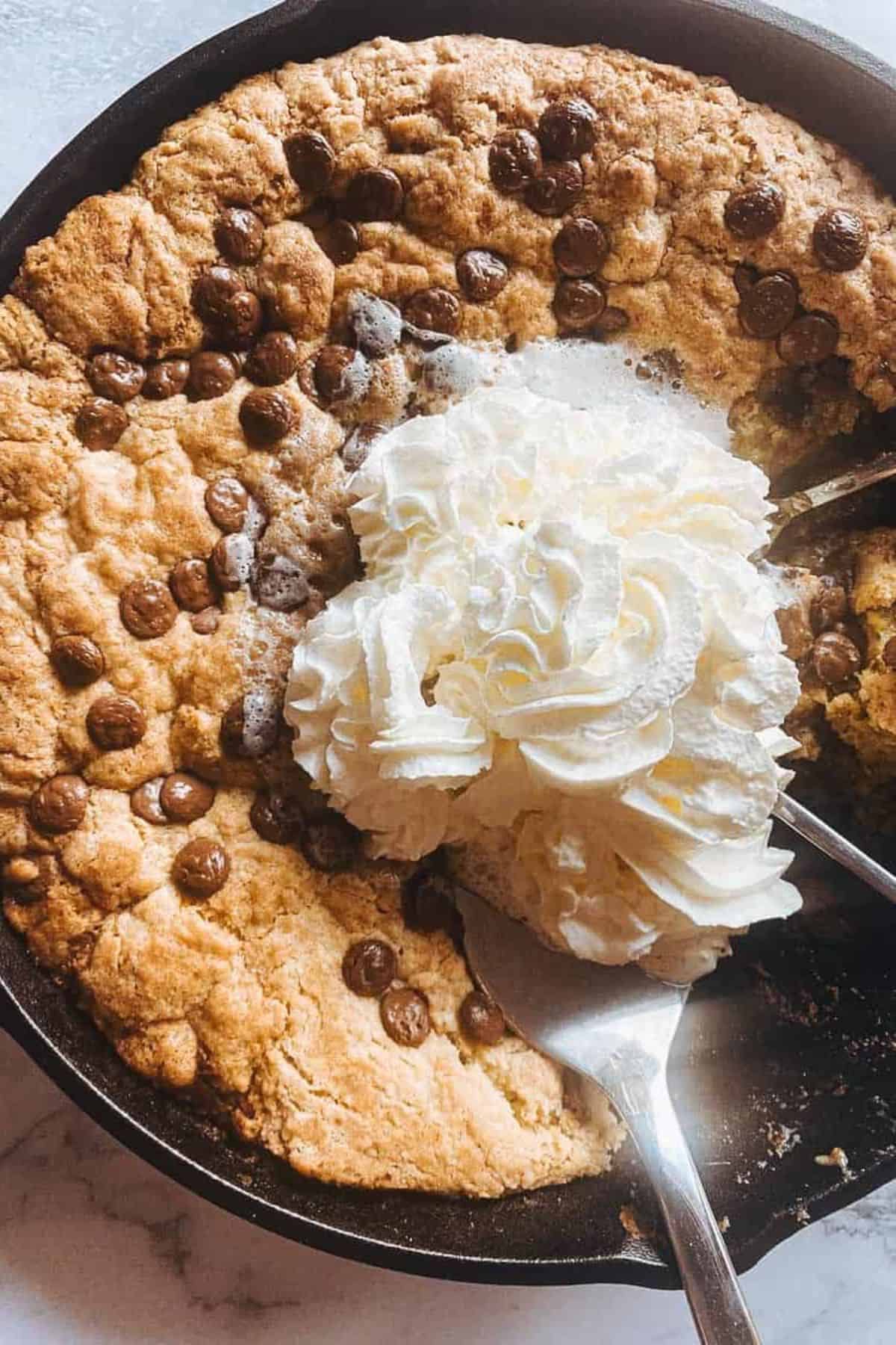 Chocolate chip cookie in a skillet topped with a scoop of vanilla ice cream.
