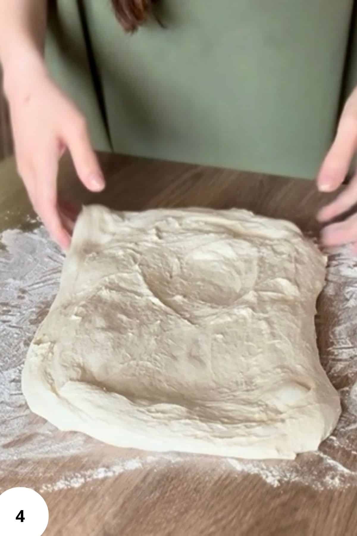 Person flattening dough on a floured surface.