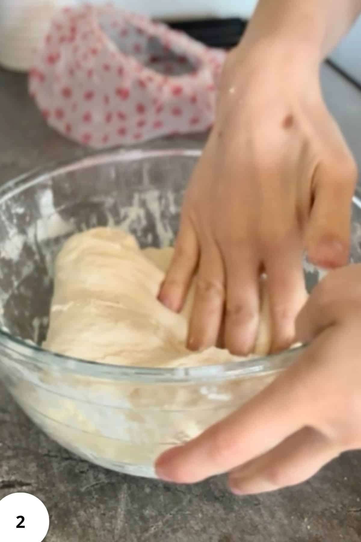 Person performing the stretch and fold technique on dough inside a mixing bowl.