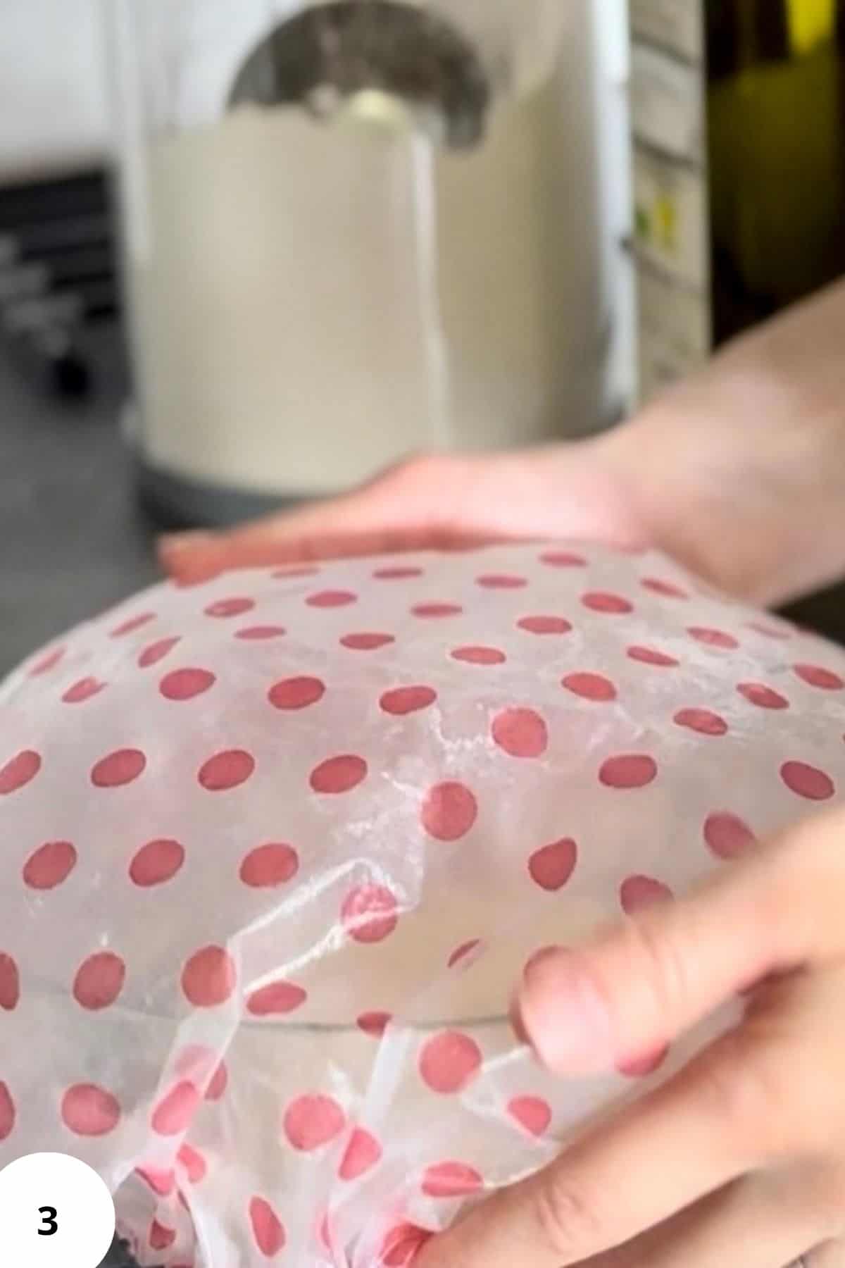 Person covering a bowl with a round sheet of dough, preparing for resting or rising.