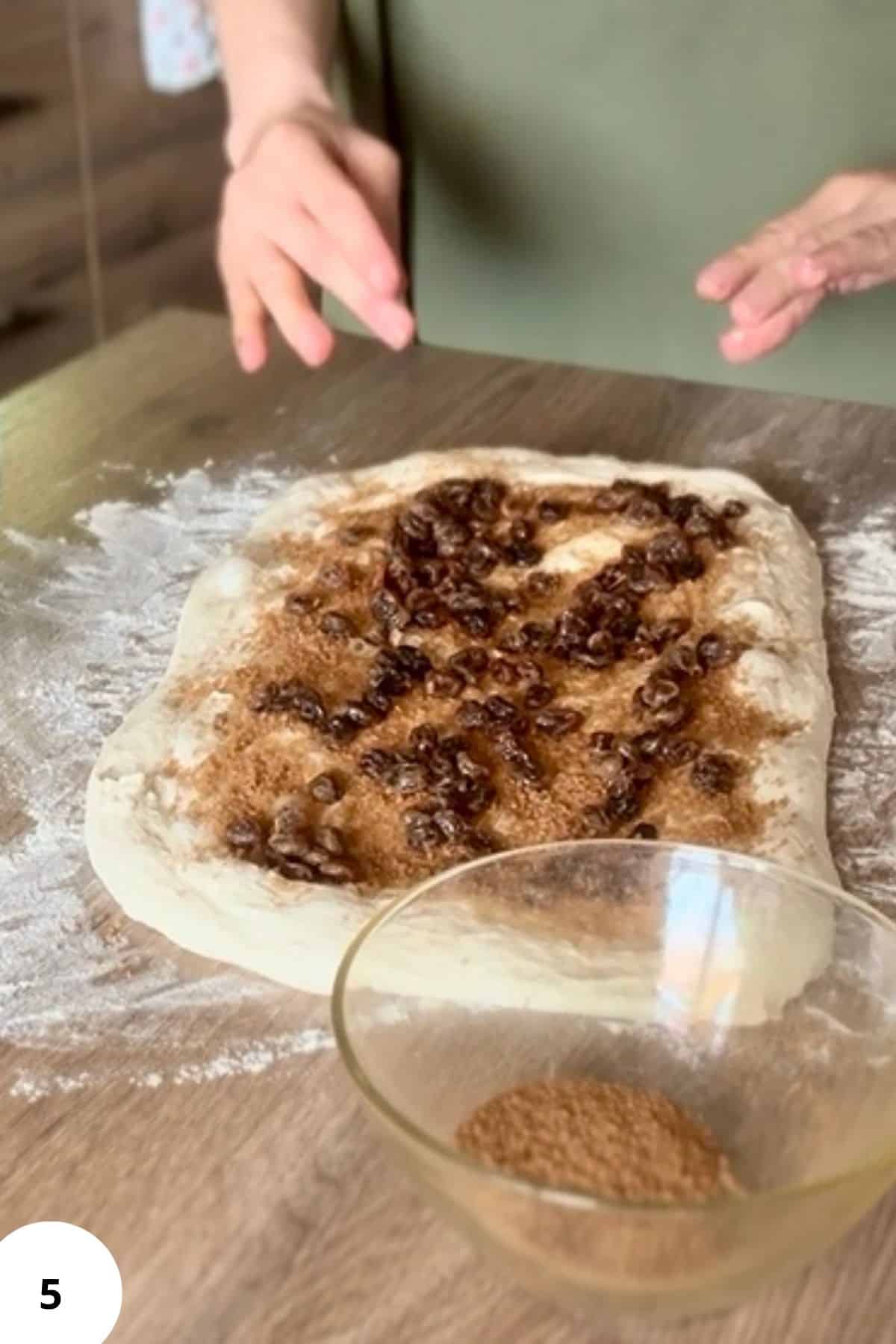 Person standing in front of flattened dough, spreading filling evenly across the surface.