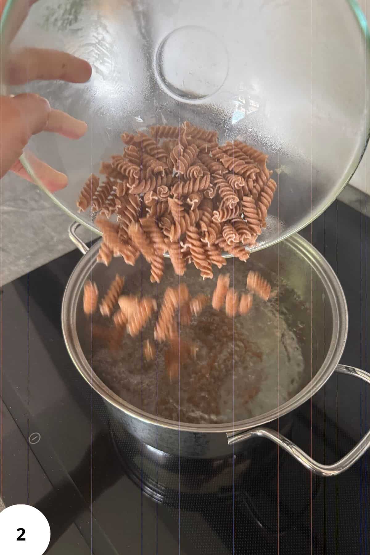 Person pouring dry pasta into a pot of boiling water on the stove.