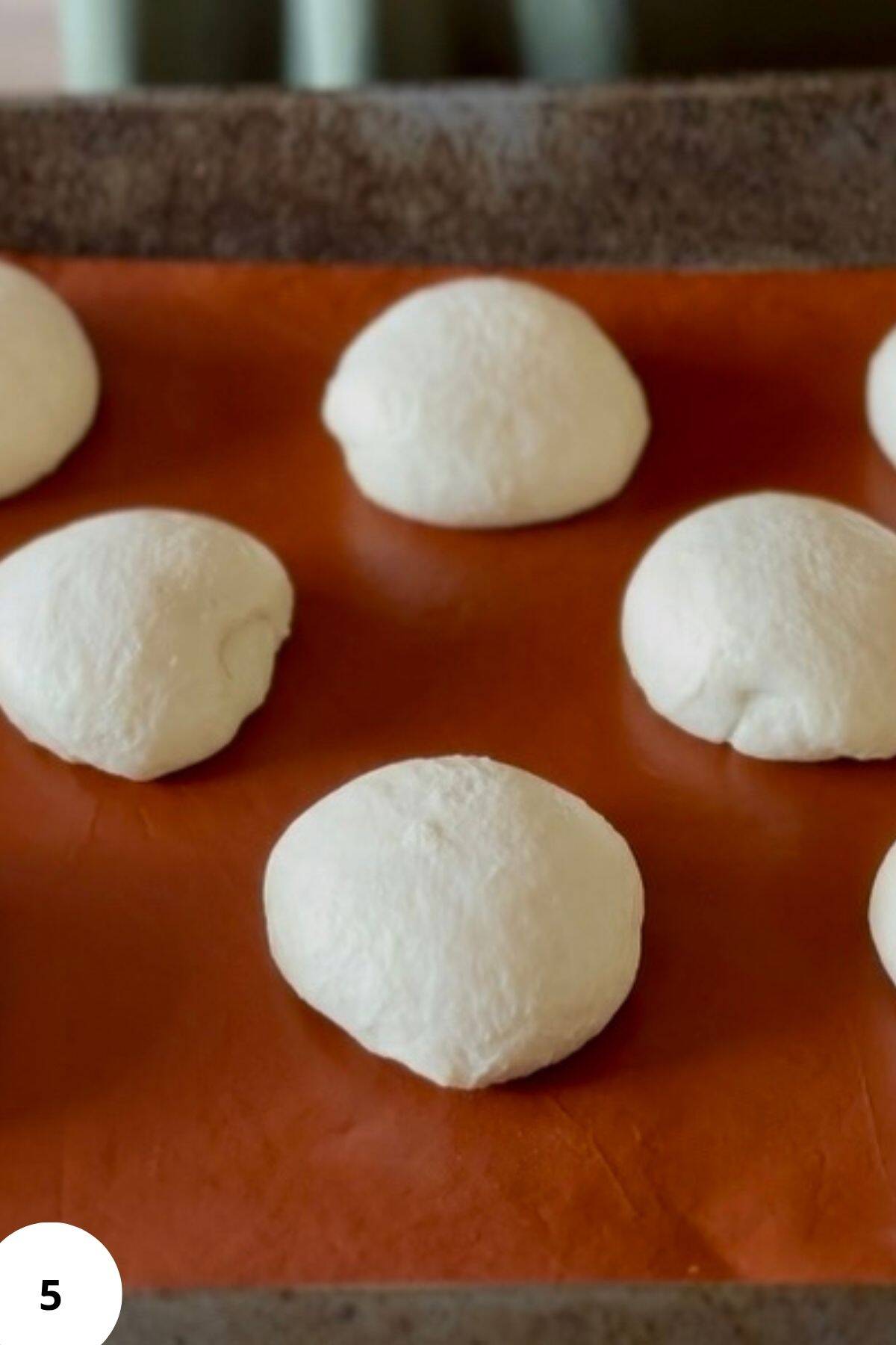 Unbaked burger bun on a parchment-lined tray.