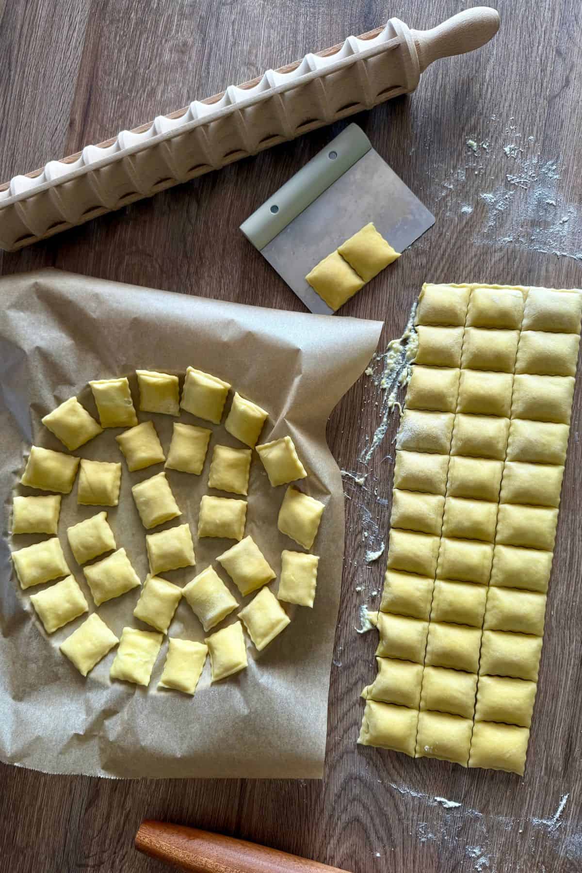Uncut sheet of filled ravioli beside individual ravioli pieces arranged on a parchment-lined, circle-shaped tray.