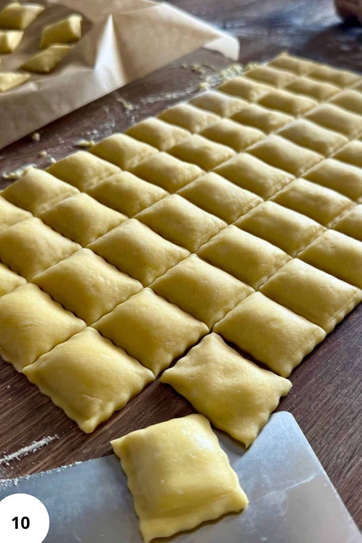 Close-up of a single ravioli being sliced from the dough sheet with a cutter.