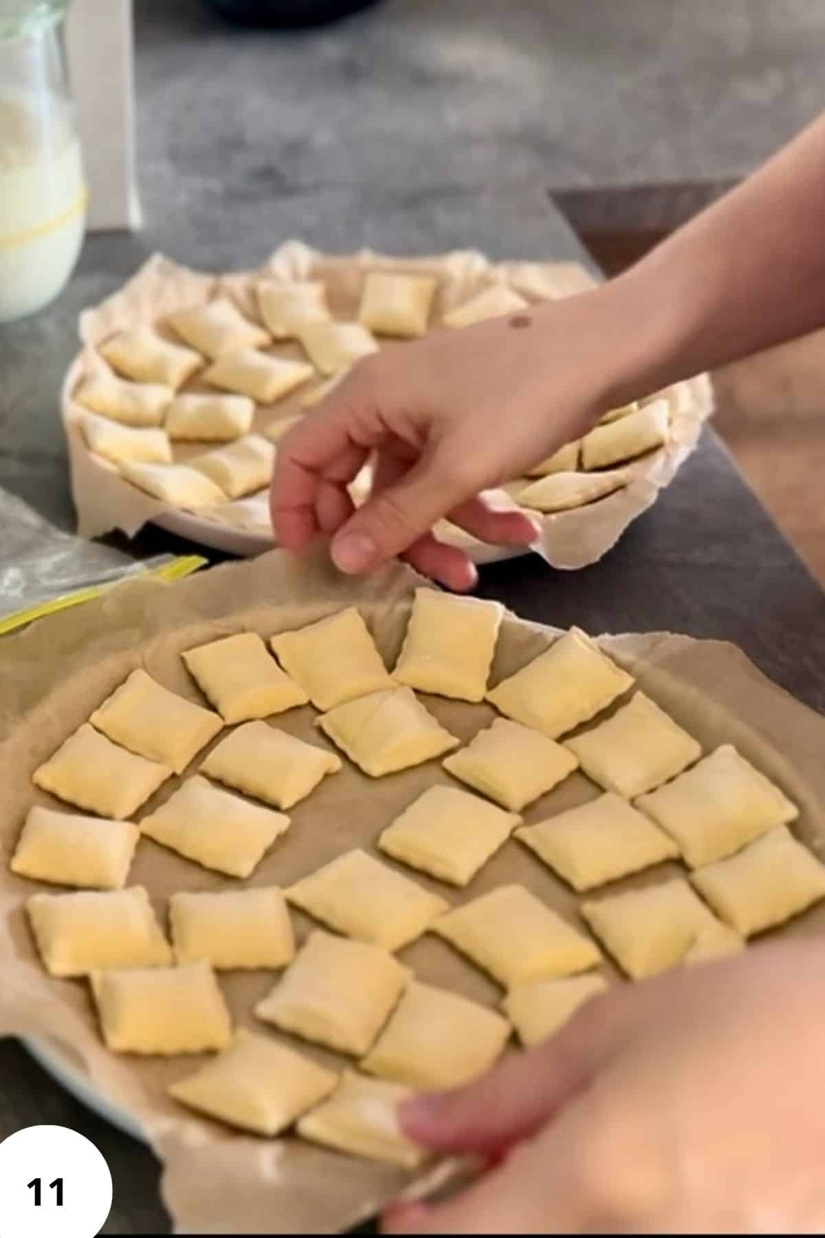 A hand placing a ravioli onto a parchment-lined, circle-shaped pan.