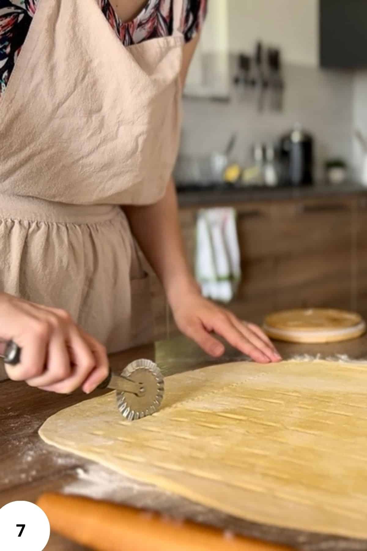 A person slicing the dough into pieces using a pastry cutter.