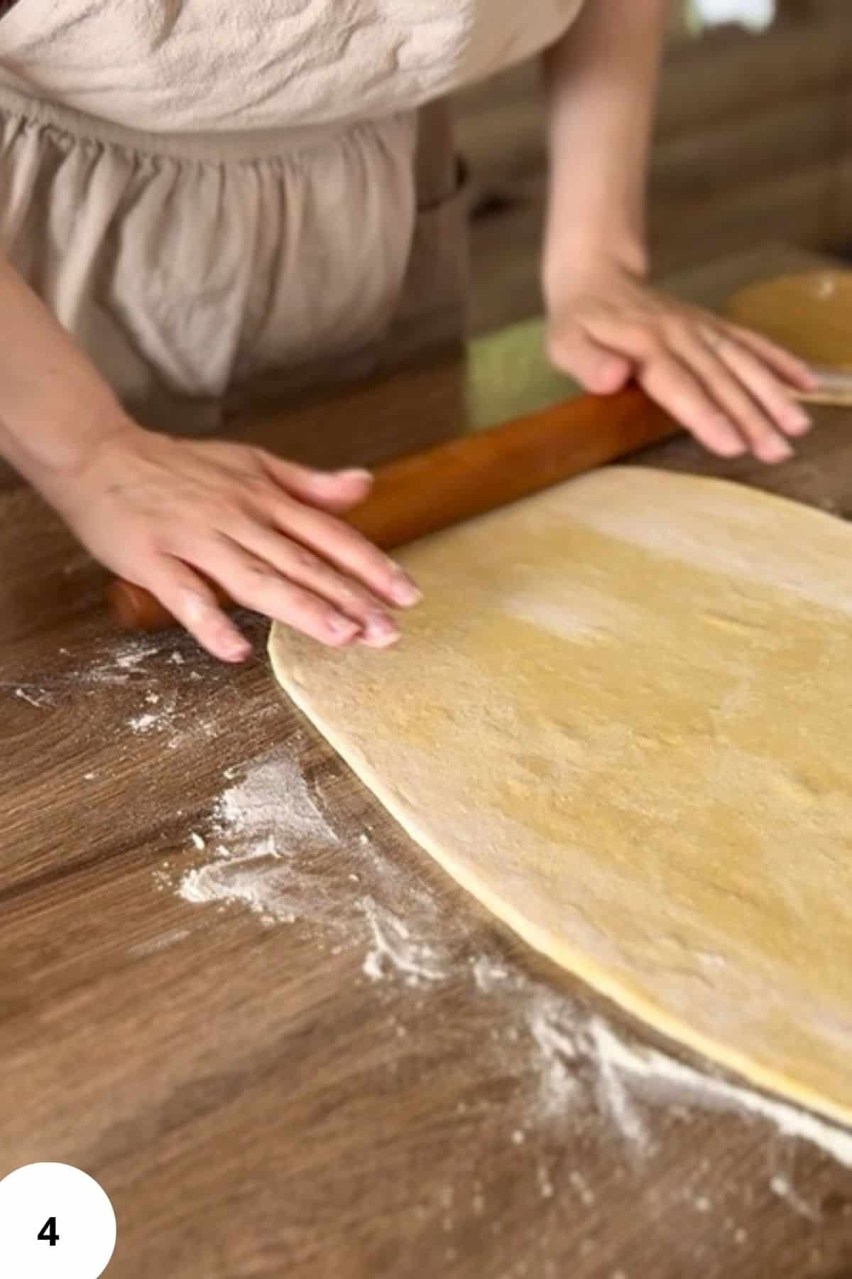 A person using a rolling pin to flatten the dough.