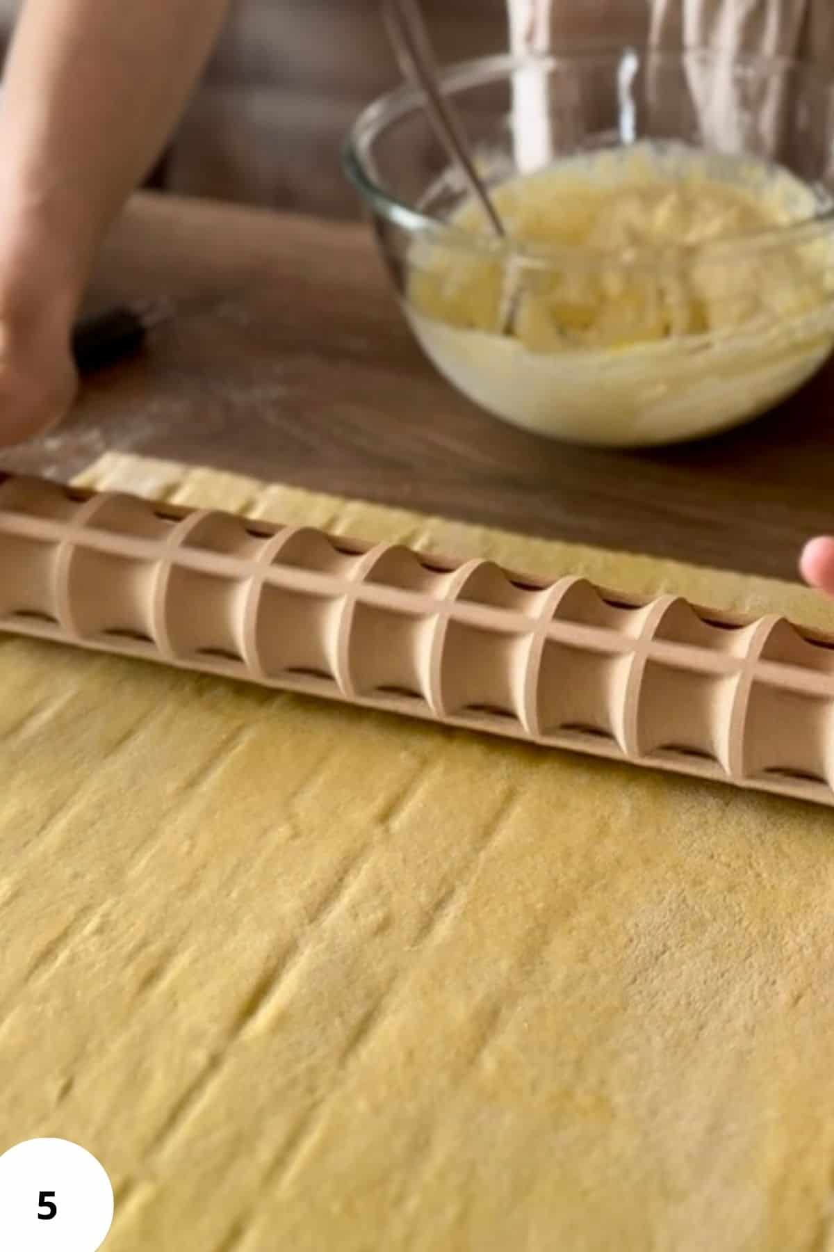 A person using a carved ravioli rolling pin to flatten and shape the dough into even squares.