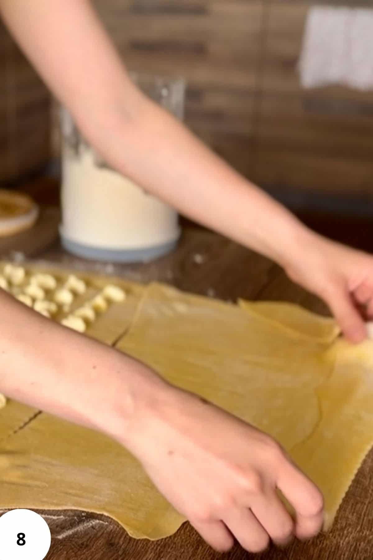 A person lifting the edge of the dough to fold it over and cover the filling.