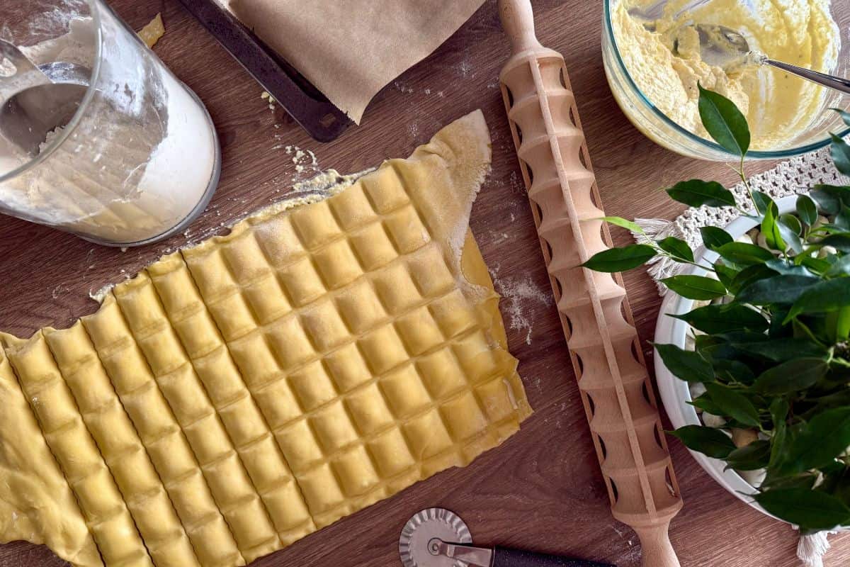 Ravioli being shaped on a floured surface with ravioli carved shaped rolling pin.