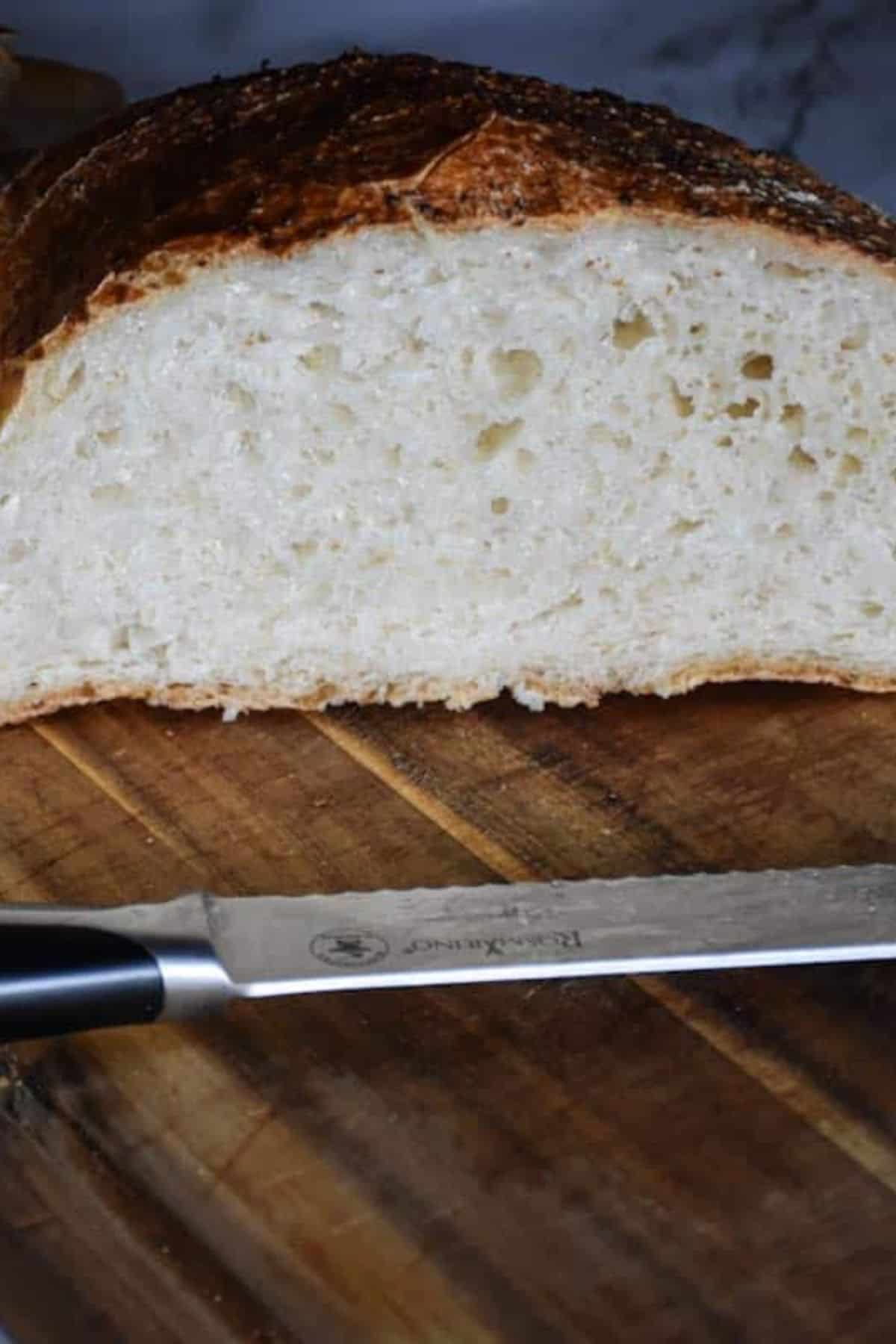 Sliced sourdough bread arranged on a wooden board with a knife resting beside it.
