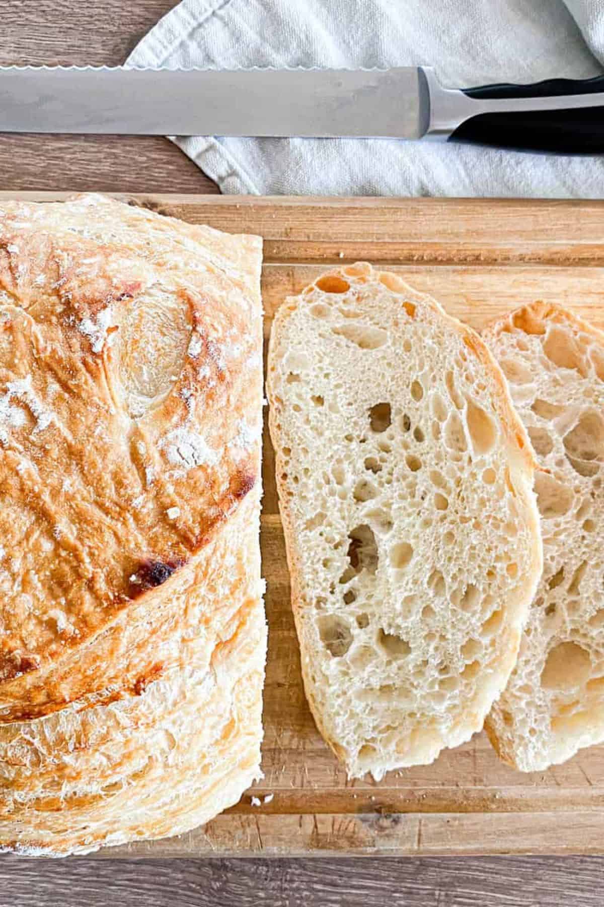Sourdough bread being sliced on a wooden board.