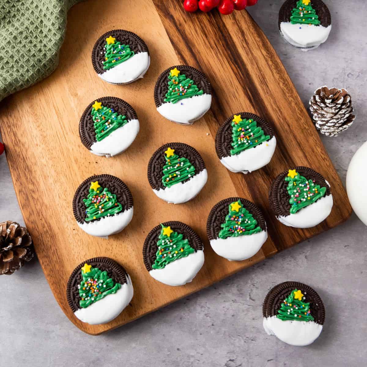 Christmas Tree Oreo cookies on a wooden board, placed on a cloth and surrounded by Christmas decorations.