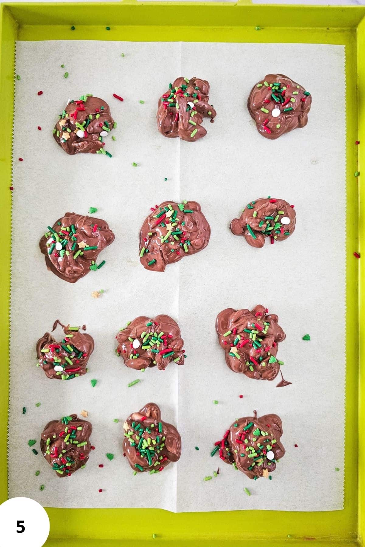 Dropping portions of melted chocolate and nuts from a scooper onto parchment-lined baking sheets for holiday candy.