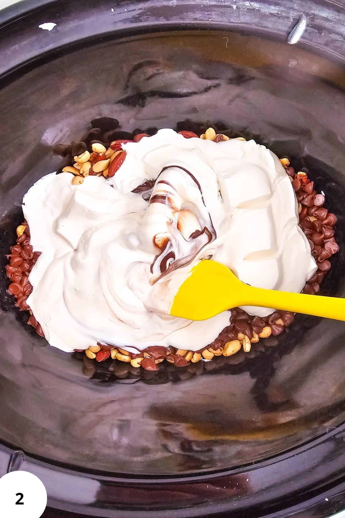 Chocolate melting in a Crockpot with mixed nuts and white almond bark for holiday candy.