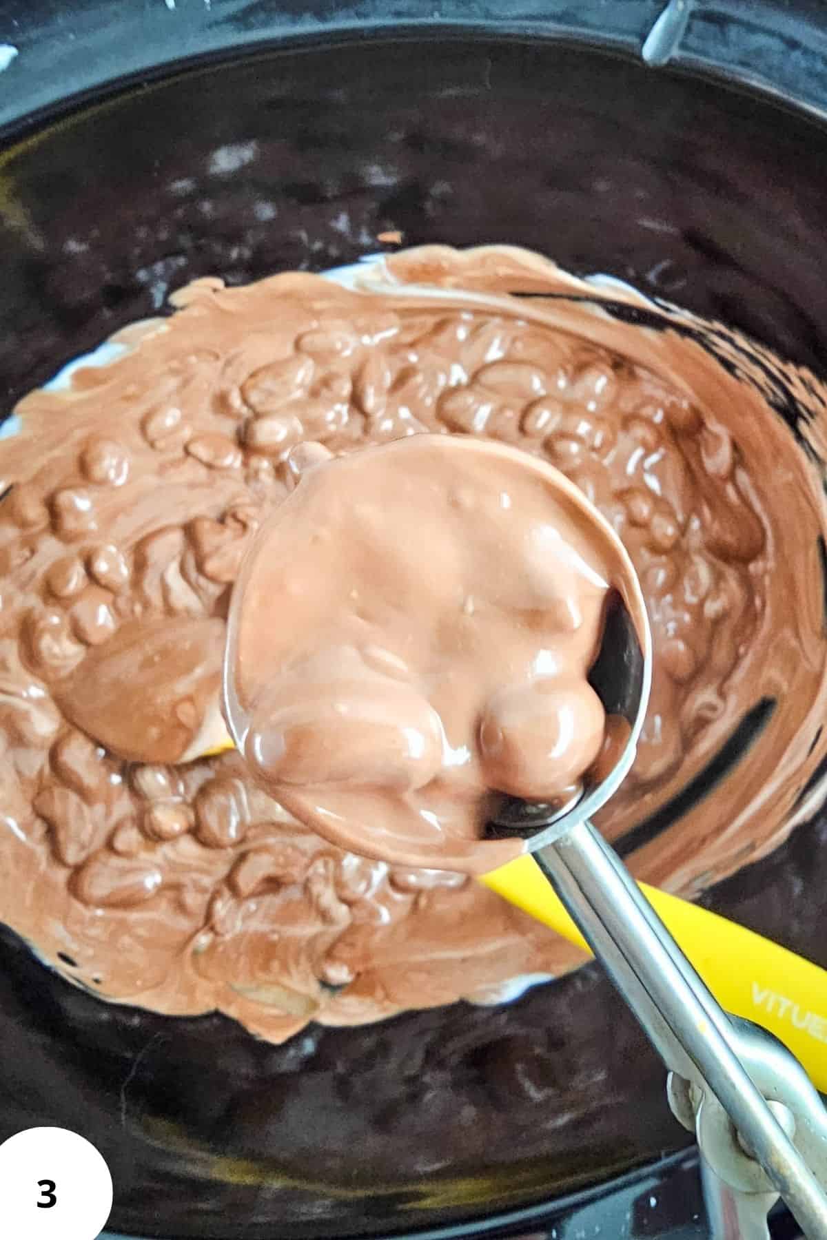 scooper holding melted chocolate and mixed nuts from a Crockpot.