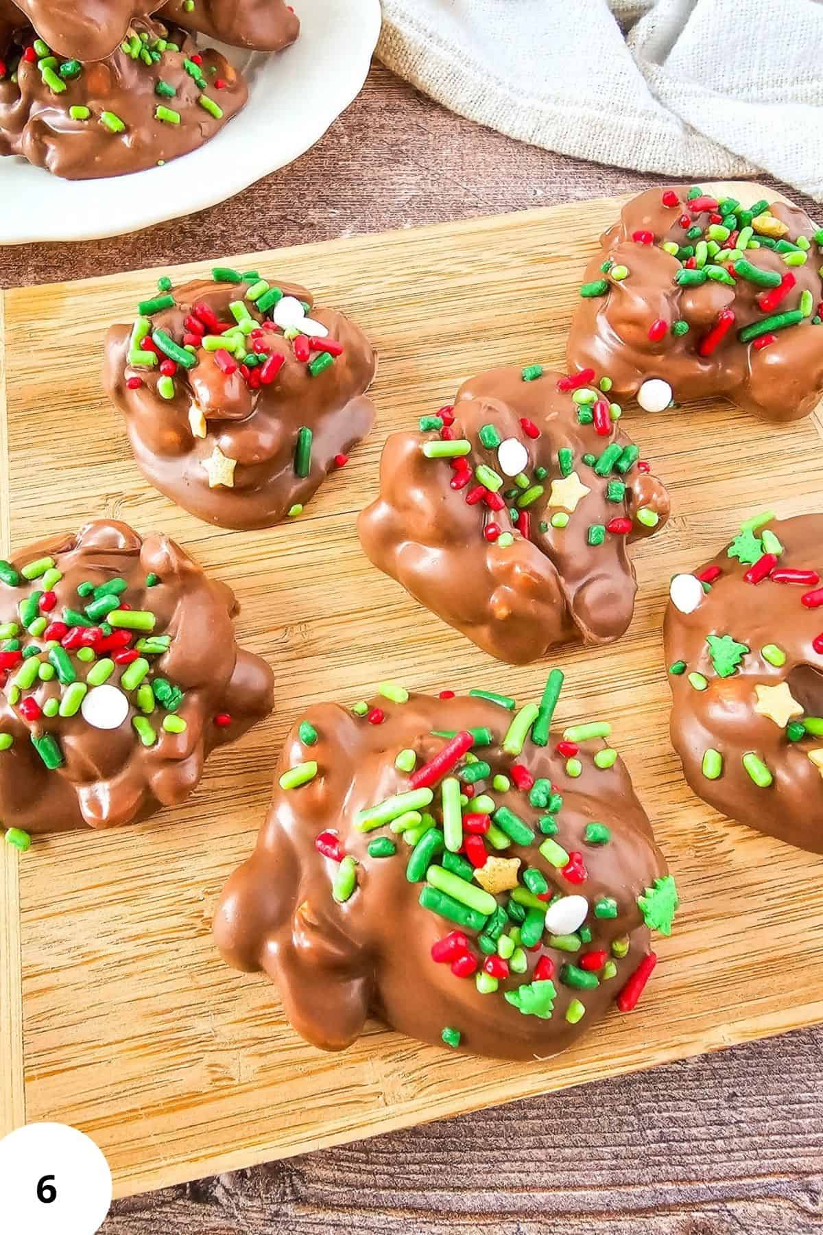 Crockpot holiday candy served on a wooden board with chocolate-coated and festive sprinkles.