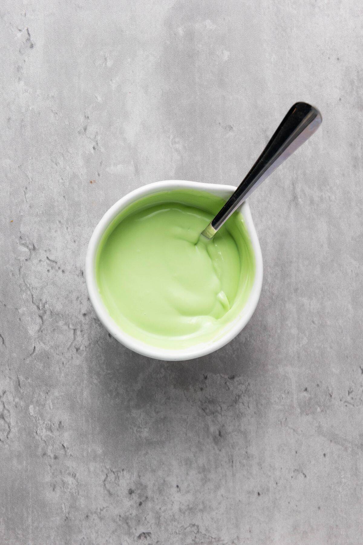 Green candy melts in a small bowl with a spoon resting inside.