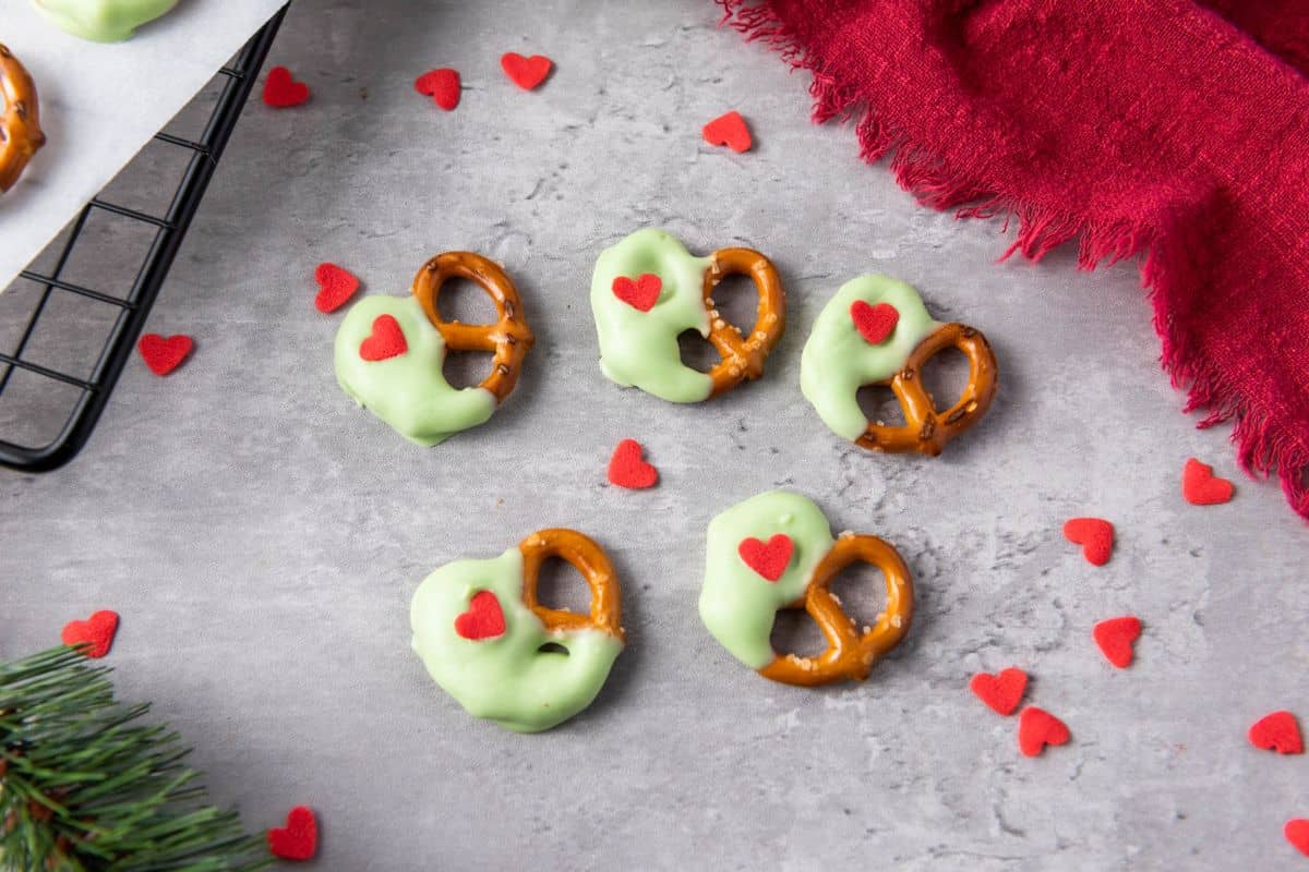 Christmas pretzels on a surface surrounded by heart sprinkles and a red cloth.