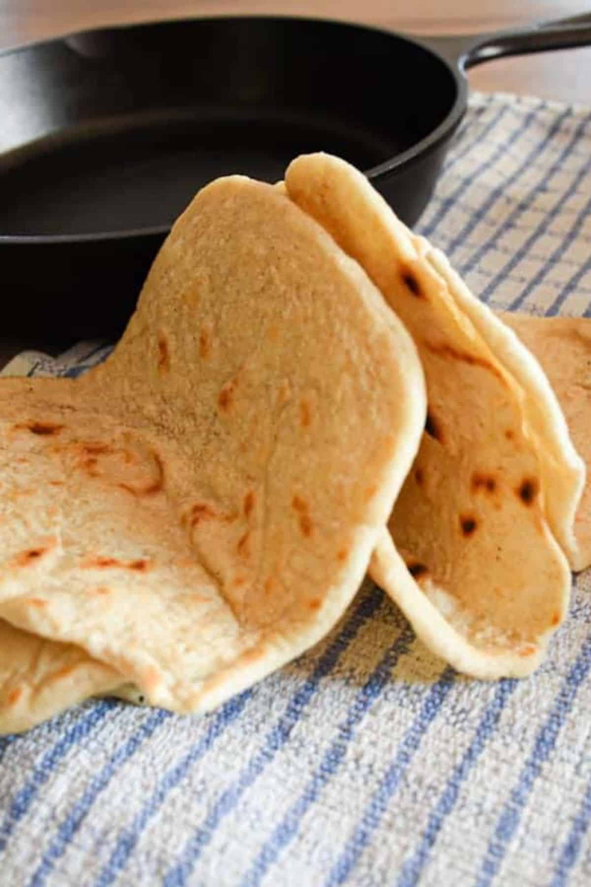 Sourdough tortillas stacked on a soft cloth, showing their light golden color and slightly rustic texture