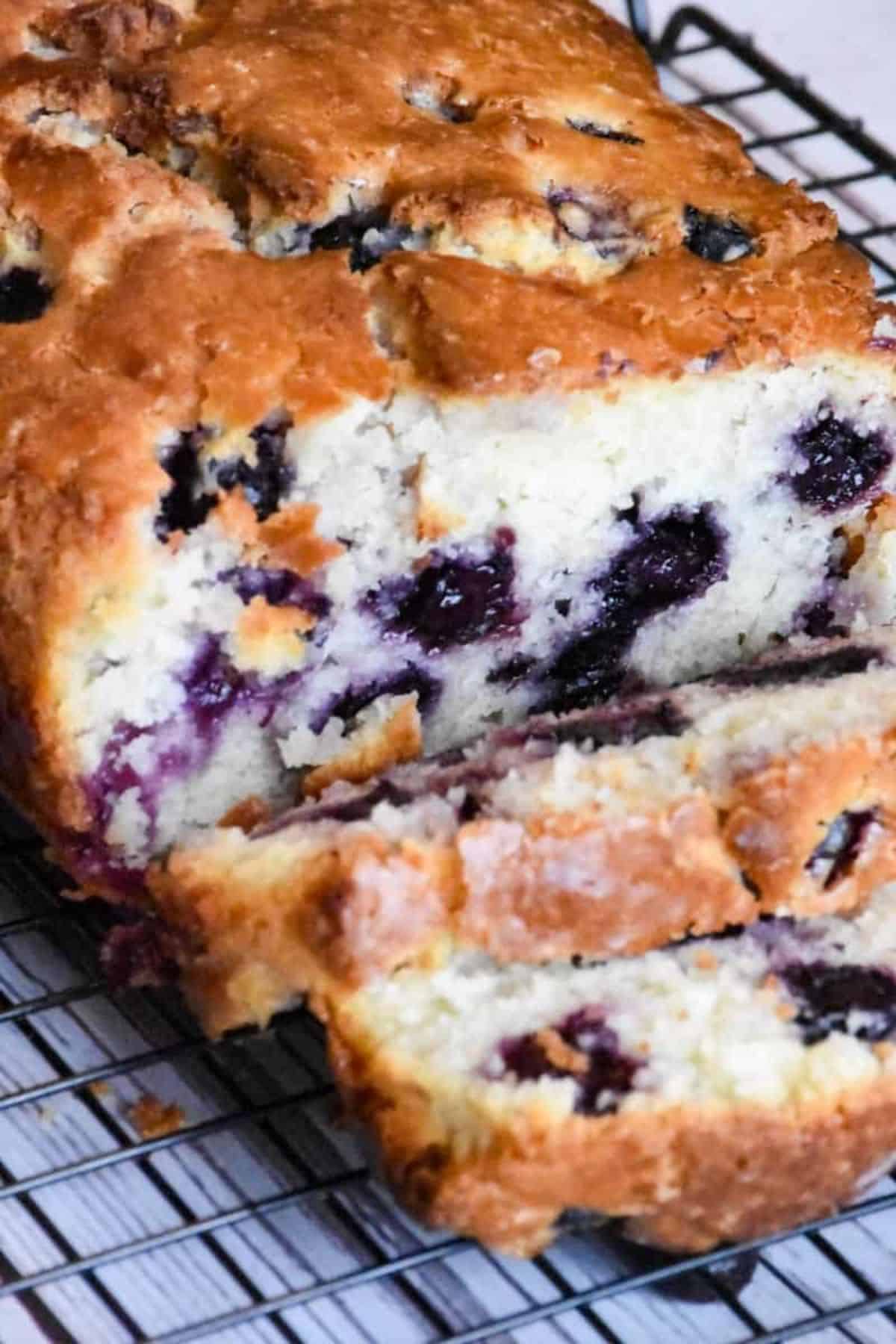 Blueberry and lemon quick bread cooling on a wire rack, with visible blueberries and a golden crust.
