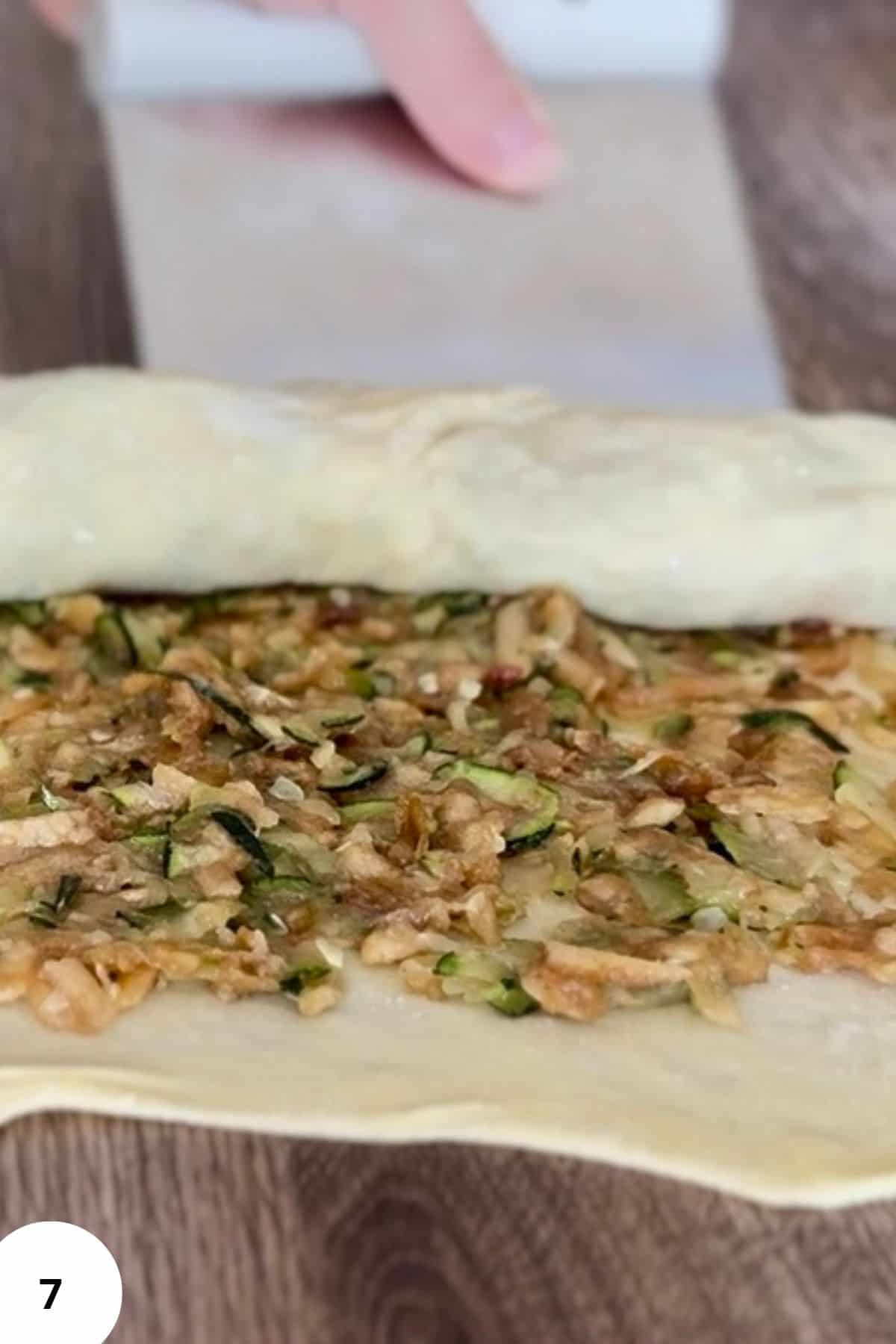 Dough being rolled up with strudel filling inside.