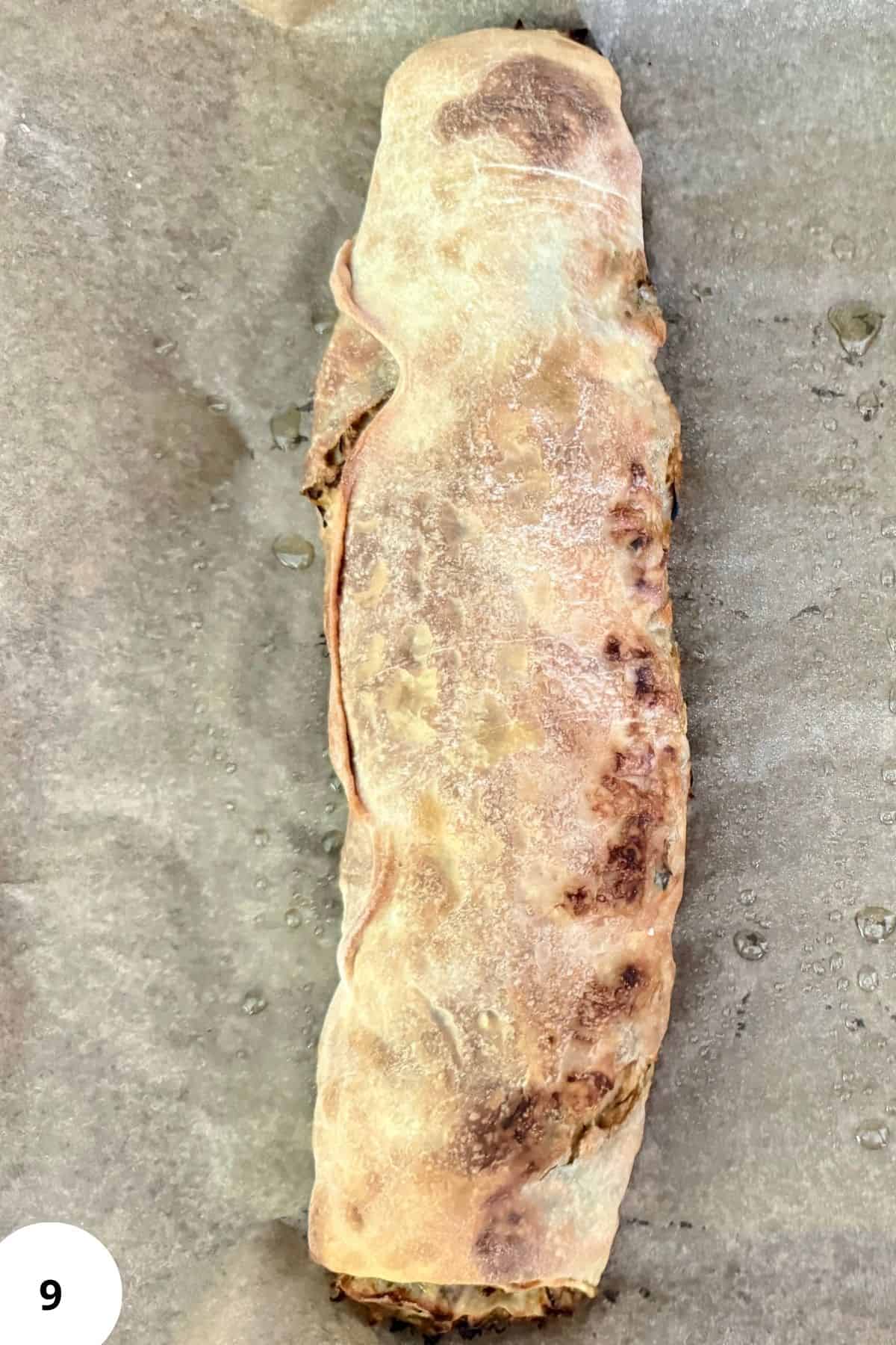 A freshly baked strudel with a golden crust resting on parchment paper.