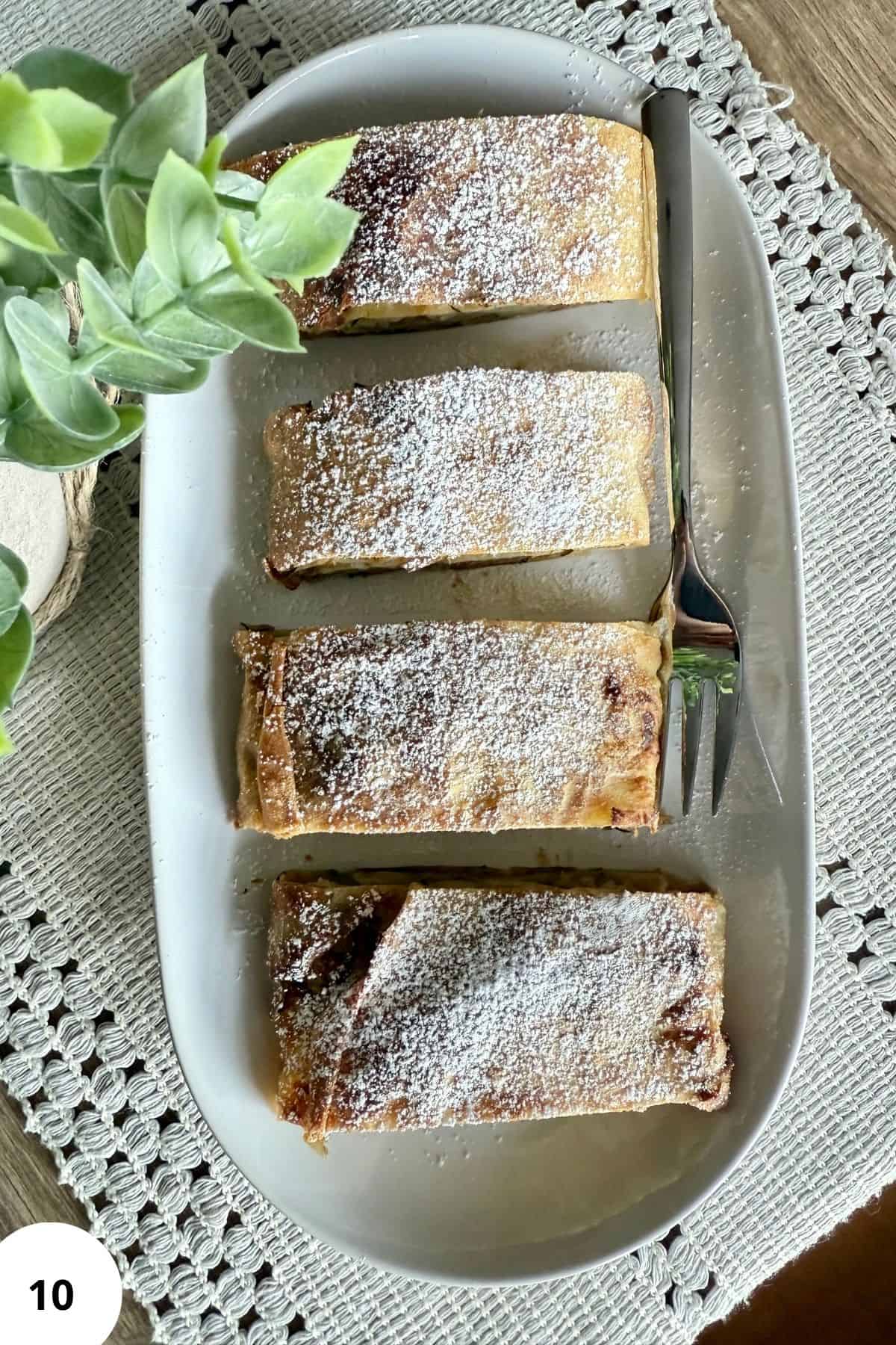 Four slices of strudel arranged on a plate with decorative plants on the side.