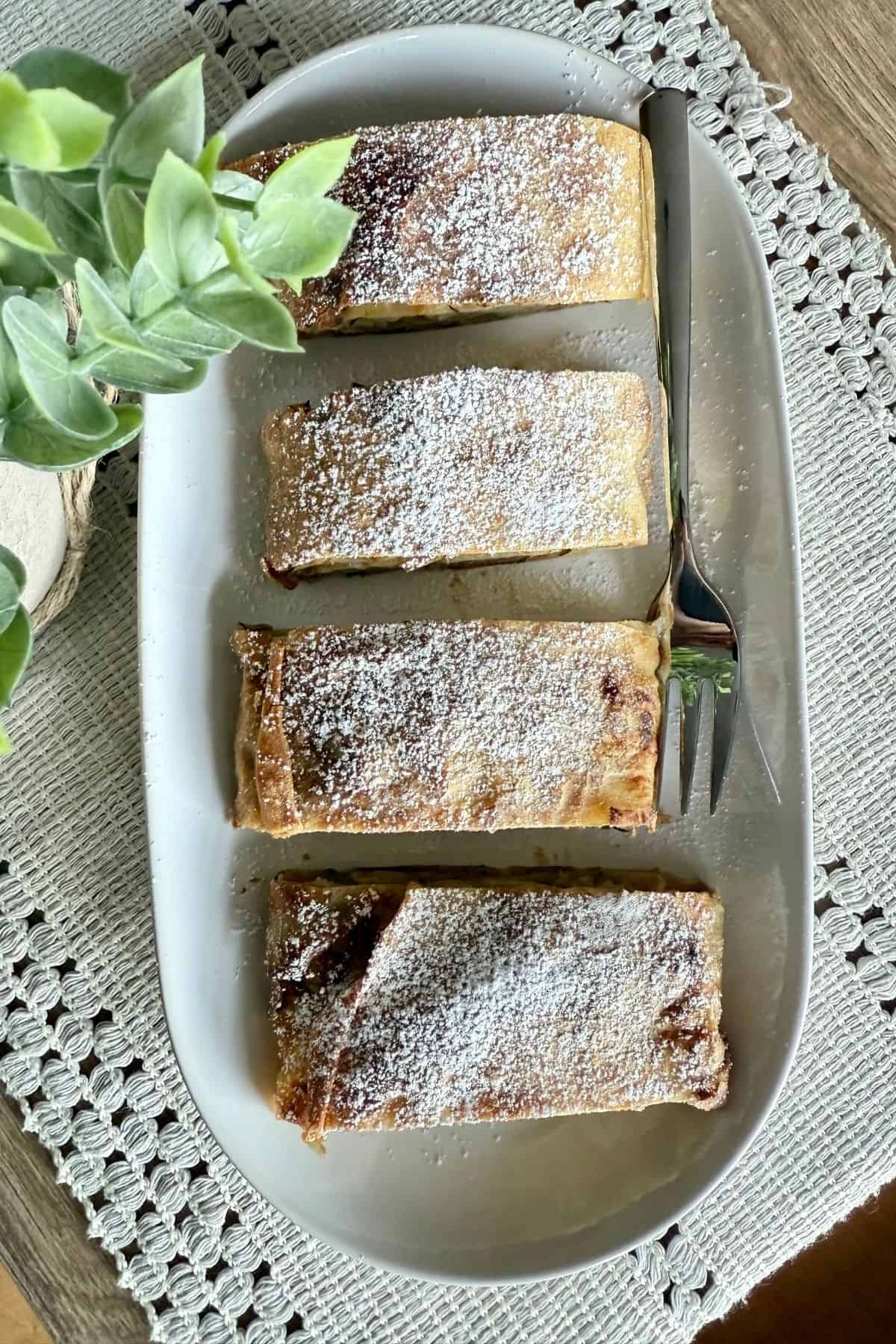 Four slices of strudel arranged on a plate with decorative plants on the side.