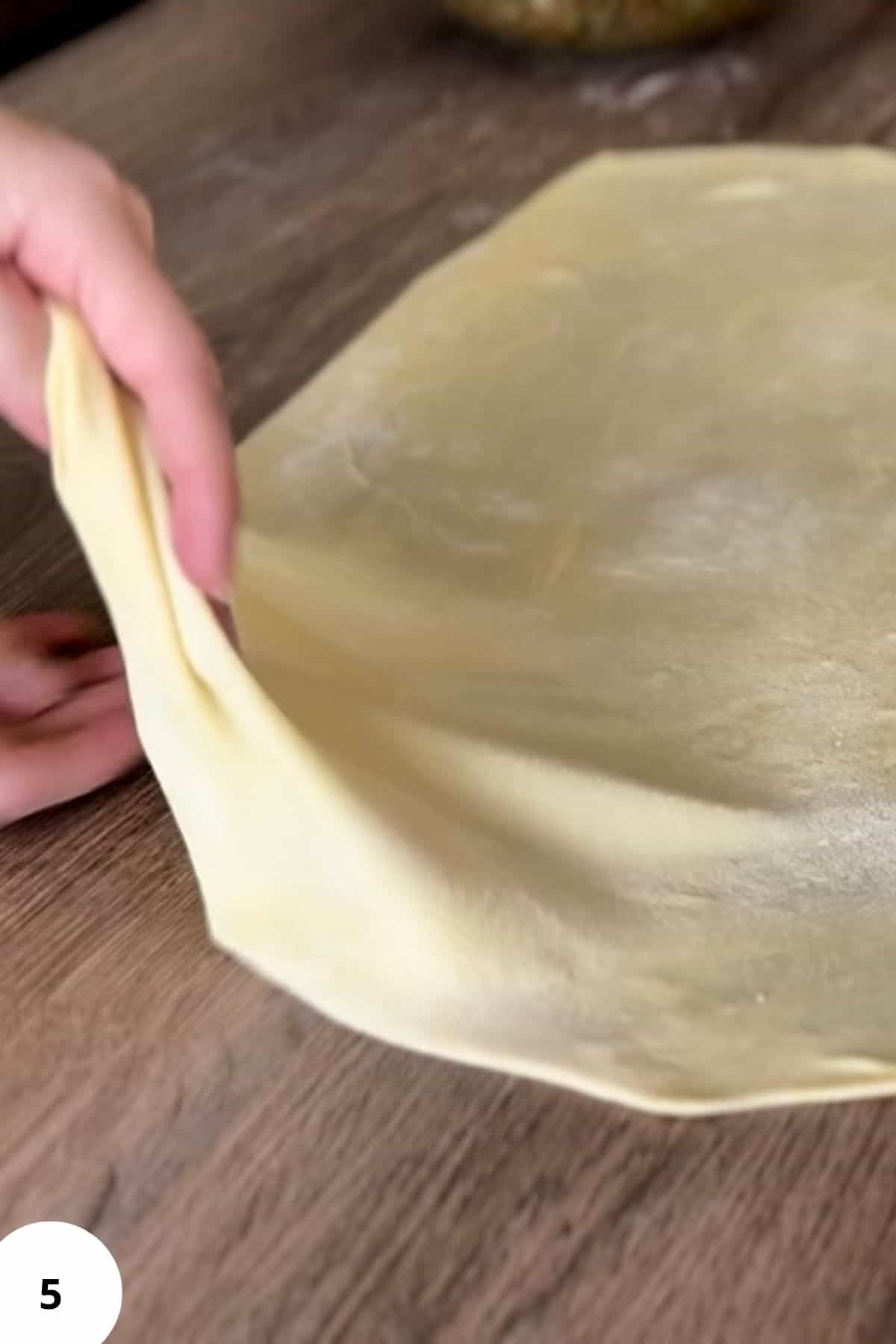 A person holding dough on a floured surface.