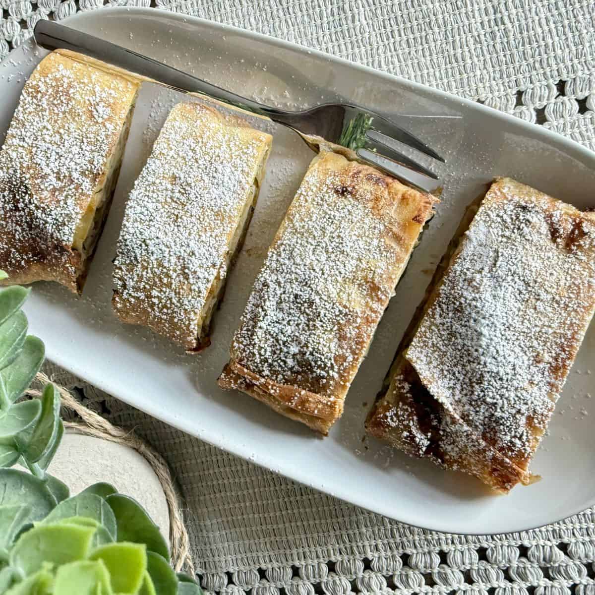 Four slices of strudel arranged on a plate with decorative plants on the side.