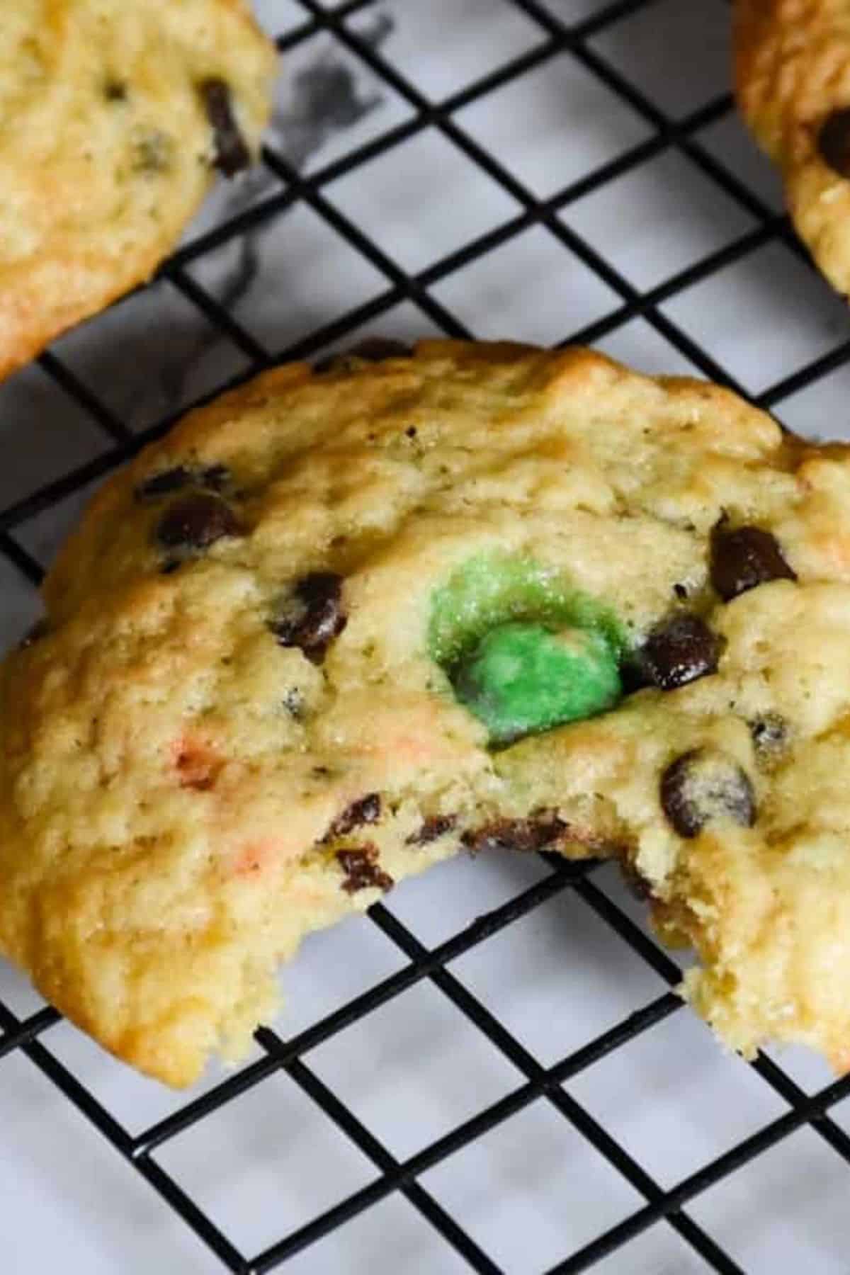 Close-up of chocolate chip cookies with visible M&Ms resting on a wire cooling rack.