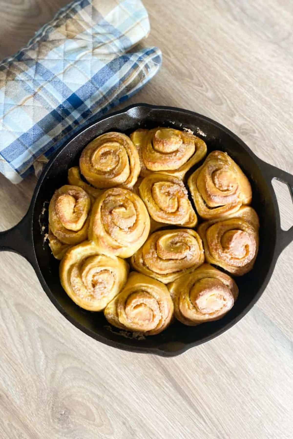 Cinnamon rolls in a skillet with a cloth underneath.
