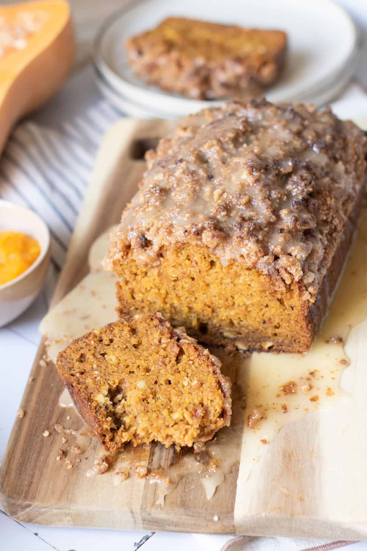 Pumpkin bread with streusel topping and honey glaze being sliced, with a plate of slices in the background.
