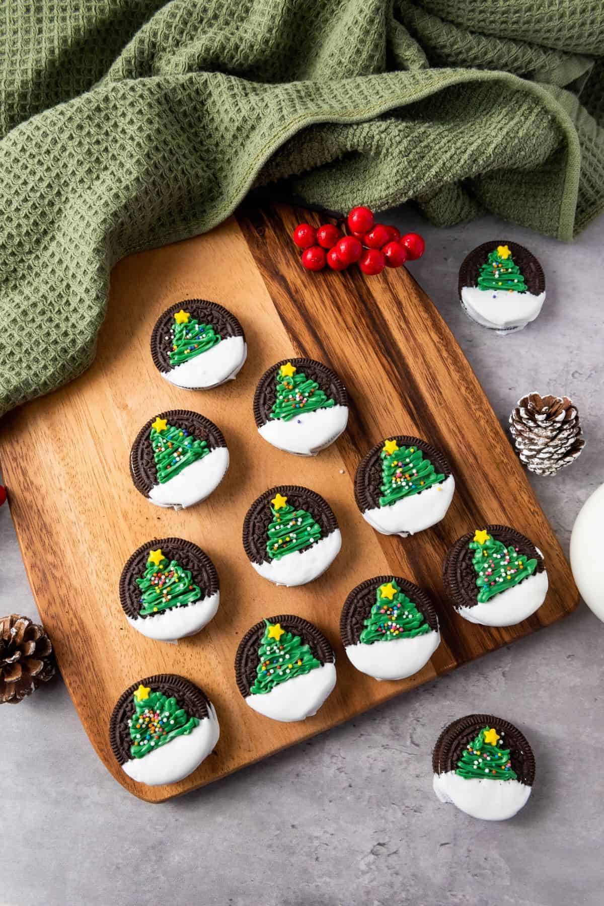 Christmas Tree Oreos arranged on a wooden board, decorated like mini Christmas trees, with a cloth placed beside them.