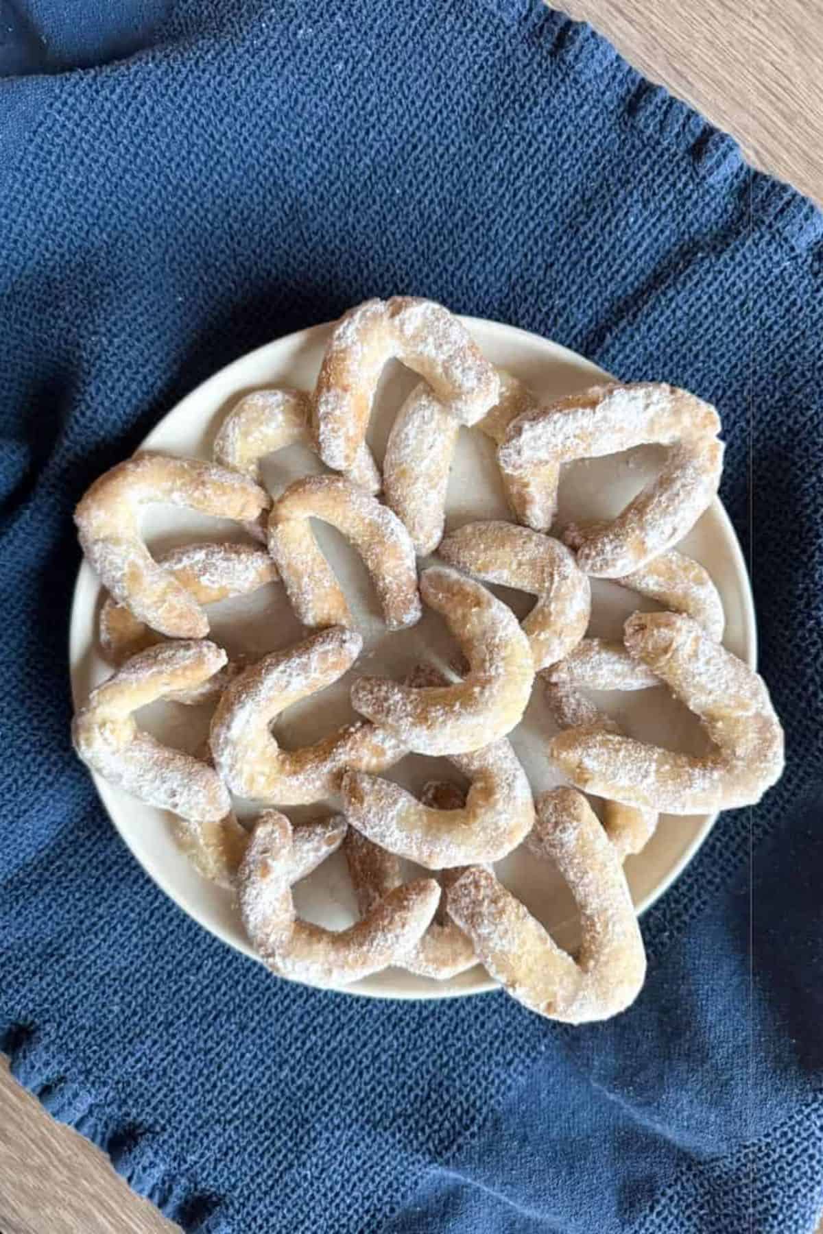 Walnut crescent cookies arranged on a plate with a cloth placed underneath.