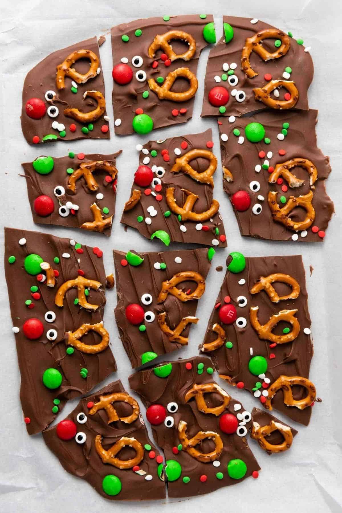 Festive reindeer chocolate bark being broken into pieces, resting on parchment paper.