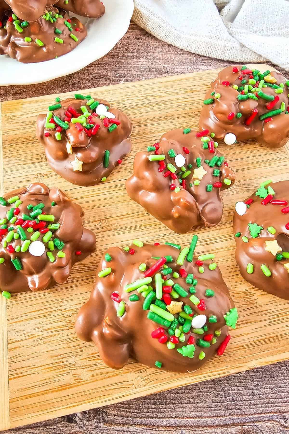 Crockpot Christmas candy topped with sprinkles, arranged on a wooden board.