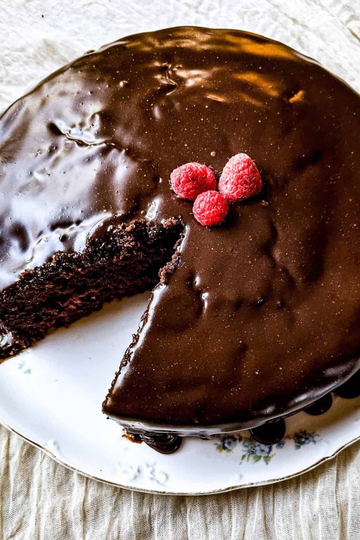 Sliced chocolate cake topped with fresh raspberries and served on a plate.