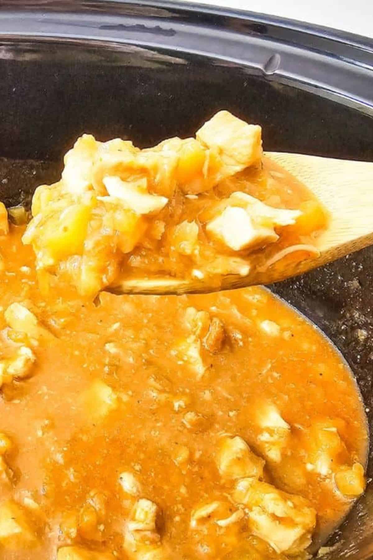 Crockpot Hawaiian Chicken being lifted from the crockpot with a spatula, showing chicken coated in pineapple and BBQ sauce.