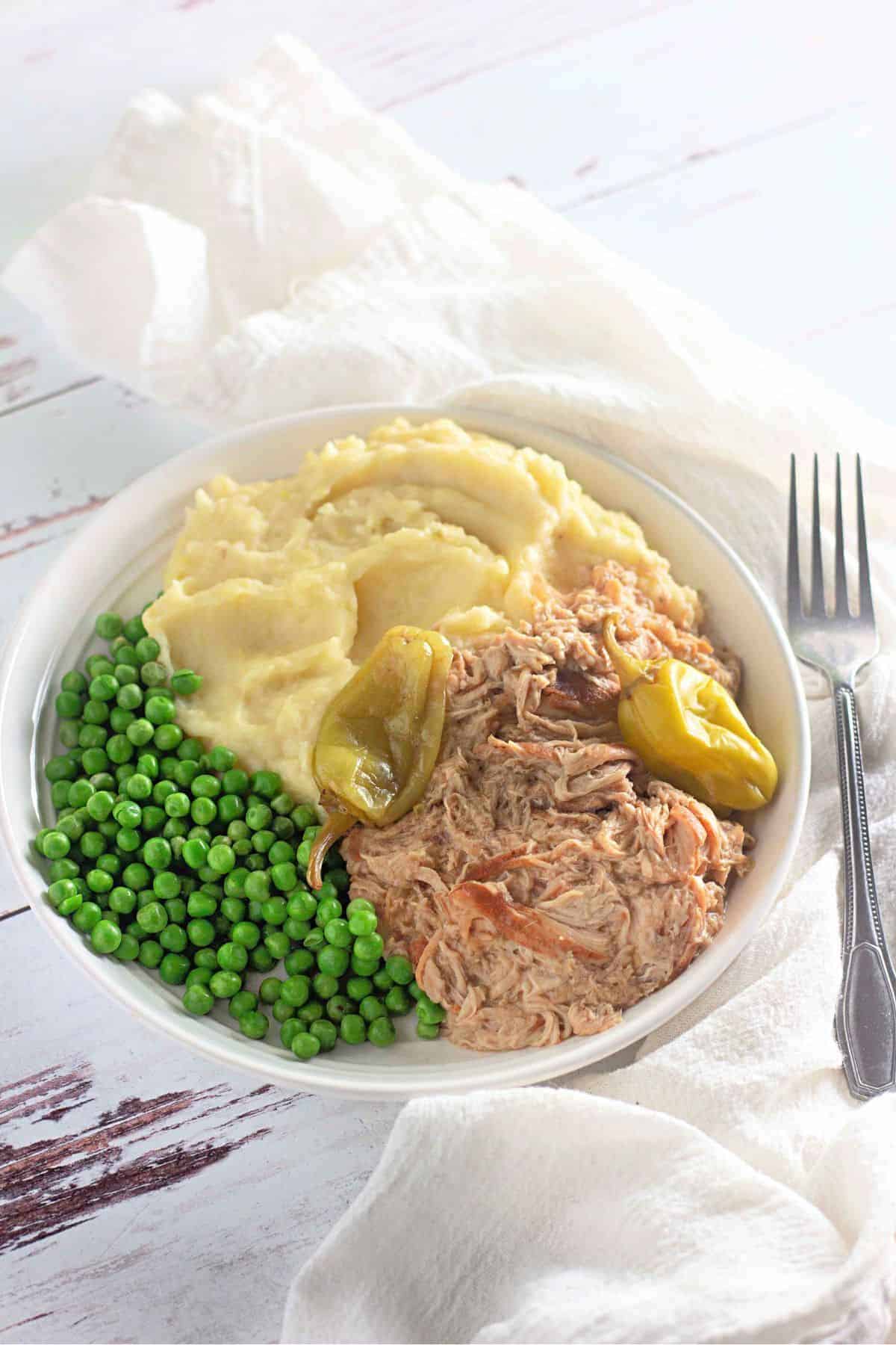 Tender Slow Cooker Mississippi Chicken served on a plate with mashed potatoes and green peas.