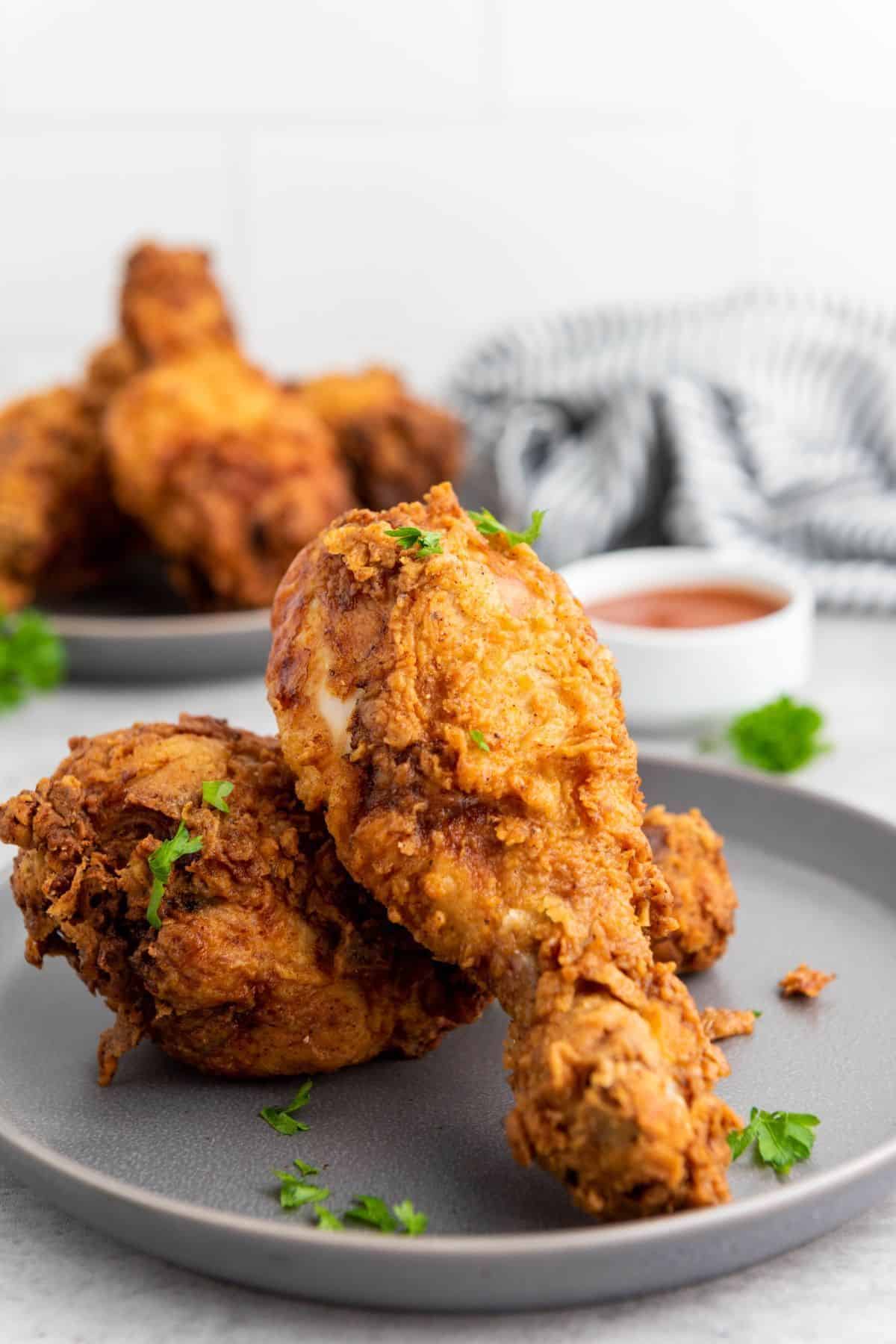 Stacked Crispy Buttermilk Fried Chicken Drumsticks on a plate with a small bowl of dipping sauce on the side.